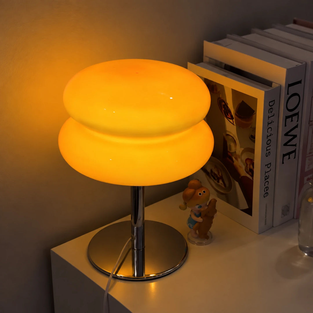 Lumi Cloud beige encendida en luz cálida sobre una mesilla, junto a unos libros y una figurita