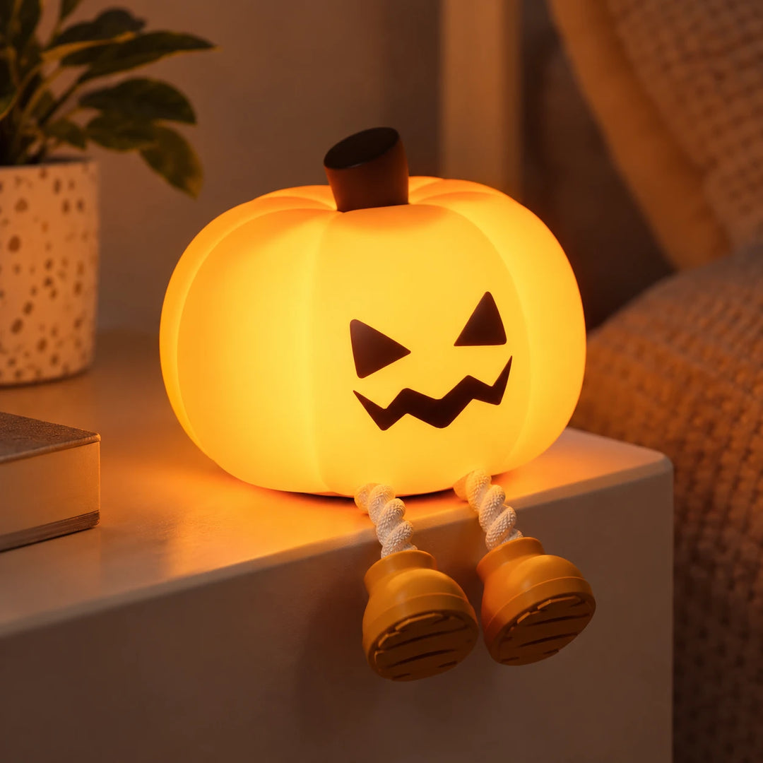 Lámpara calabaza de silicona con cara traviesa encendida junto a unos libros